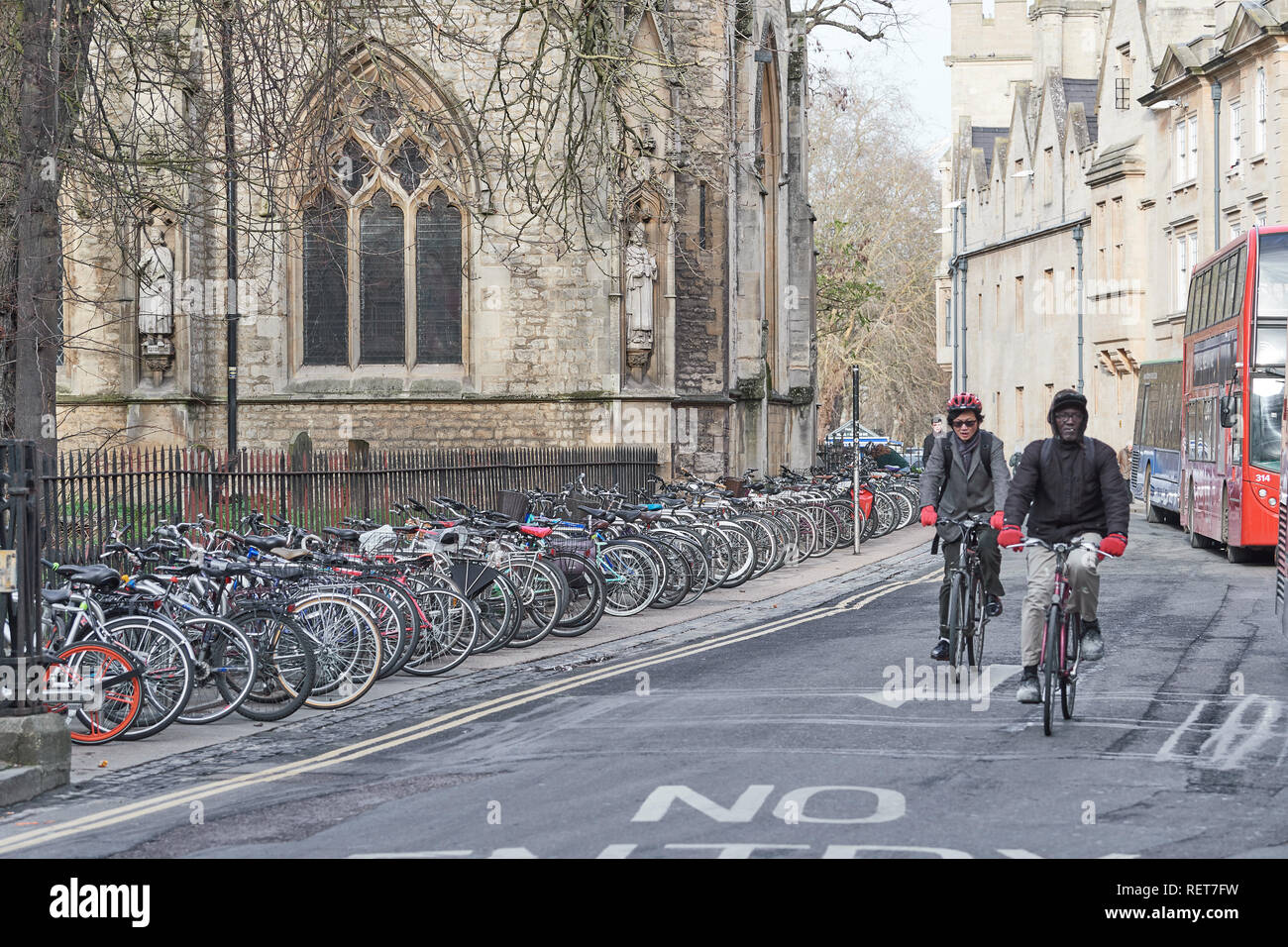 Two male students cycle along Magdalen Street East between Balliol and bicycles parked in an orderly line outside St Mary Magdalen Stock Photo
