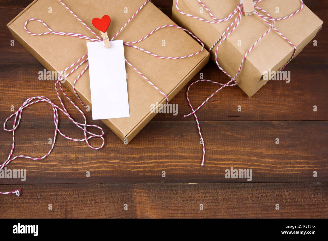 top view cardboard box with clothpin with red heart and empty white label with place for text on a brown wooden background Stock Photo