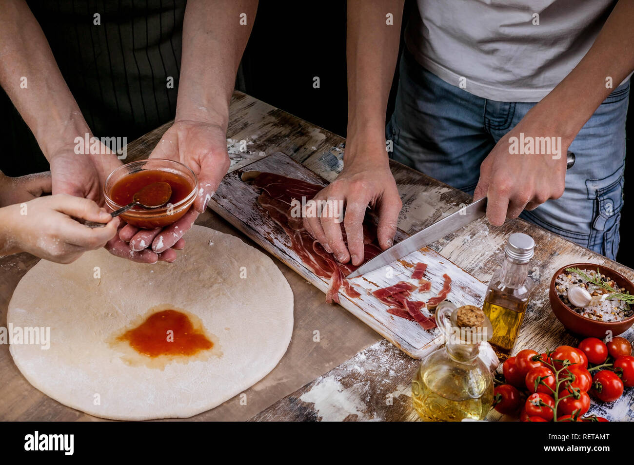 Women's and children's hand preparing homemade pizza together. Light toning Stock Photo