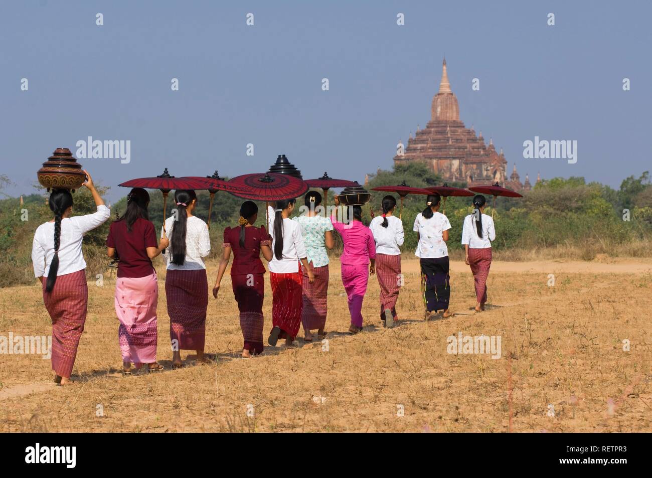 Young Burmese women with a parasol crossing a field near the Sulamani Pagoda, Bagan, Myanmar Stock Photo