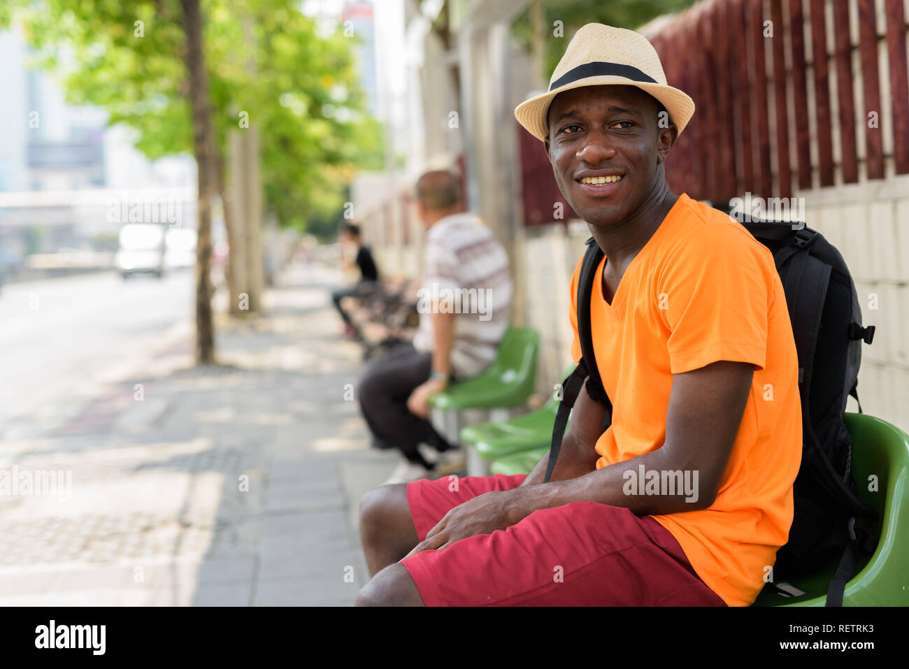 Young happy black African tourist man sitting at bus stop Stock Photo