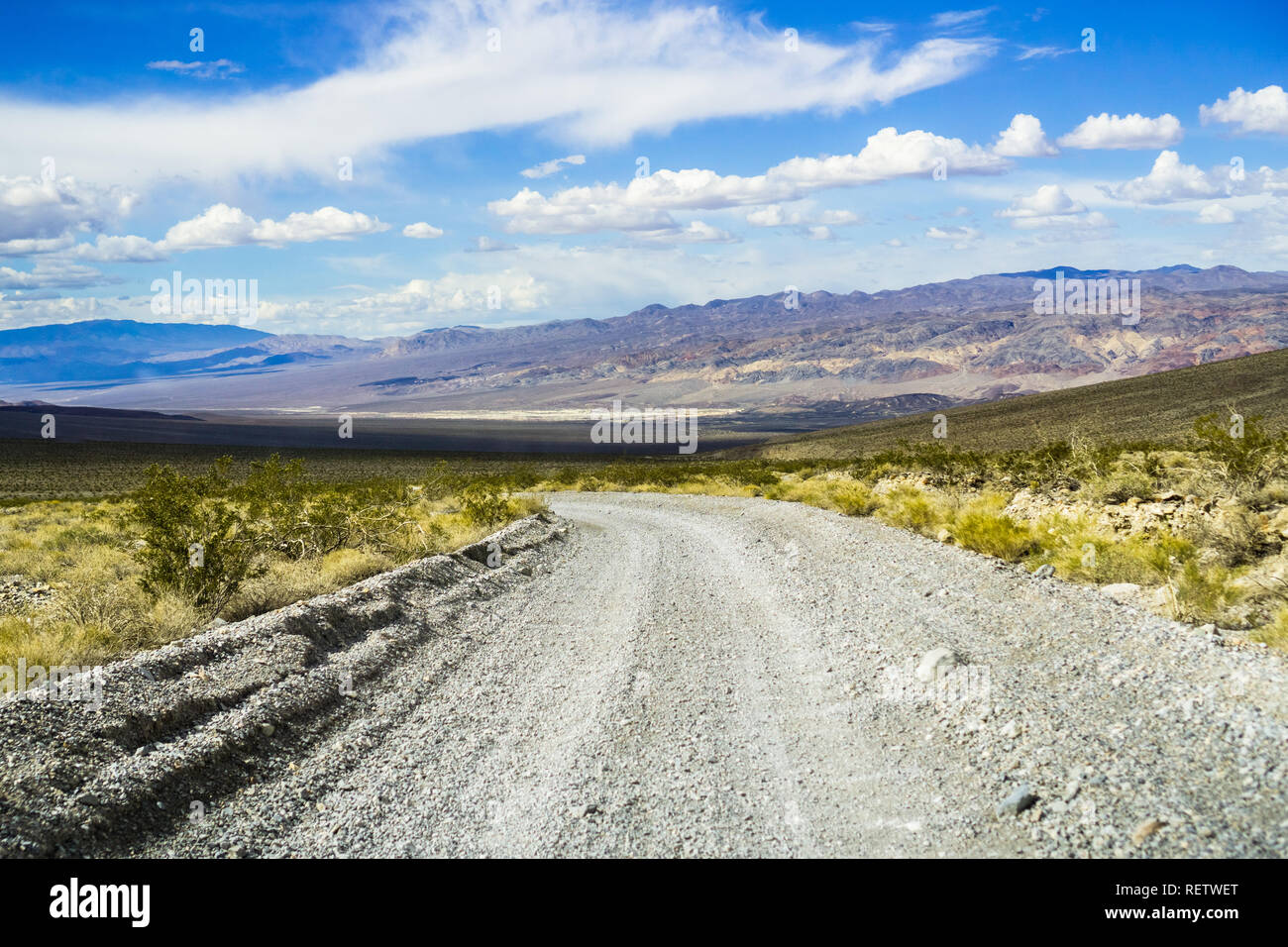 Travelling on an unpaved road through a remote area of Death Valley National Park; mountains, blue sky and white clouds in the background; California Stock Photo