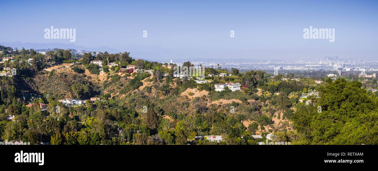 Scattered mansions on one of the hills of Bel Air neighborhood; the downtown skyscrapers visible in the background through a hazy atmosphere; Los Ange Stock Photo