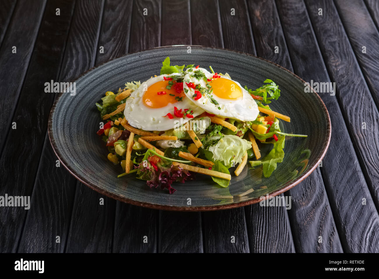 Fried eggs with avocado, salad leaves and crispy chips Stock Photo