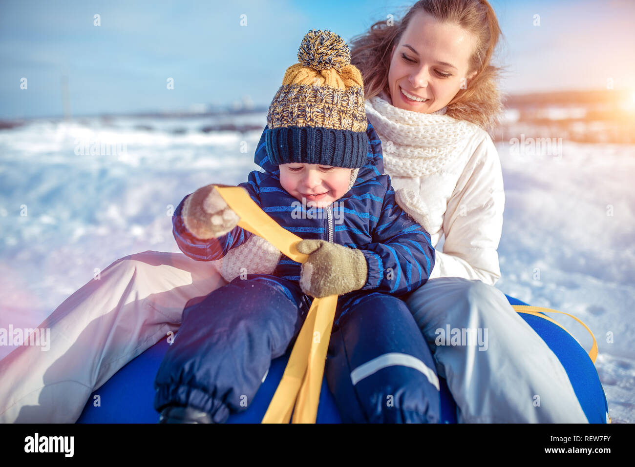Young mother woman happy smiling, sitting on tubing with her son boy 3-6 years old, playing scrabing in winter. Rest in winter morning in nature. Stock Photo