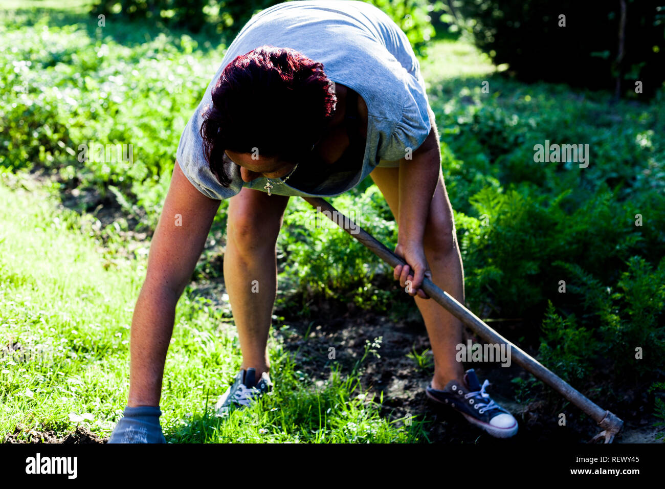 A hardworking farmer holding a gardening tool. The woman bending knees