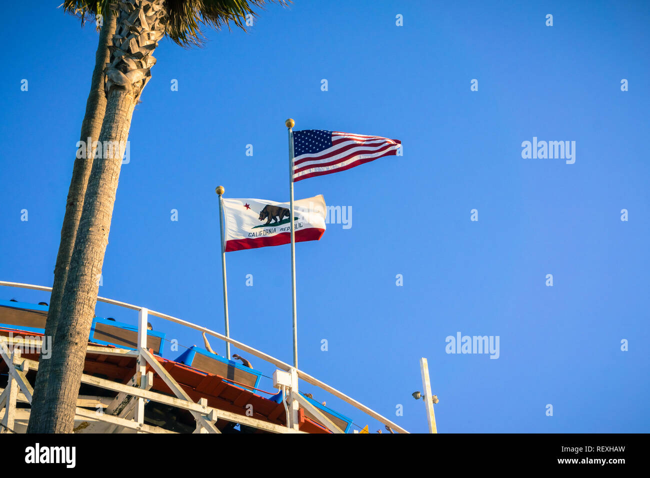 July 8, 2017 Santa Cruz/CA/USA - The USA flag and the California Republic flag blowing in the wind on top of a roller coaster on a blue sky background Stock Photo