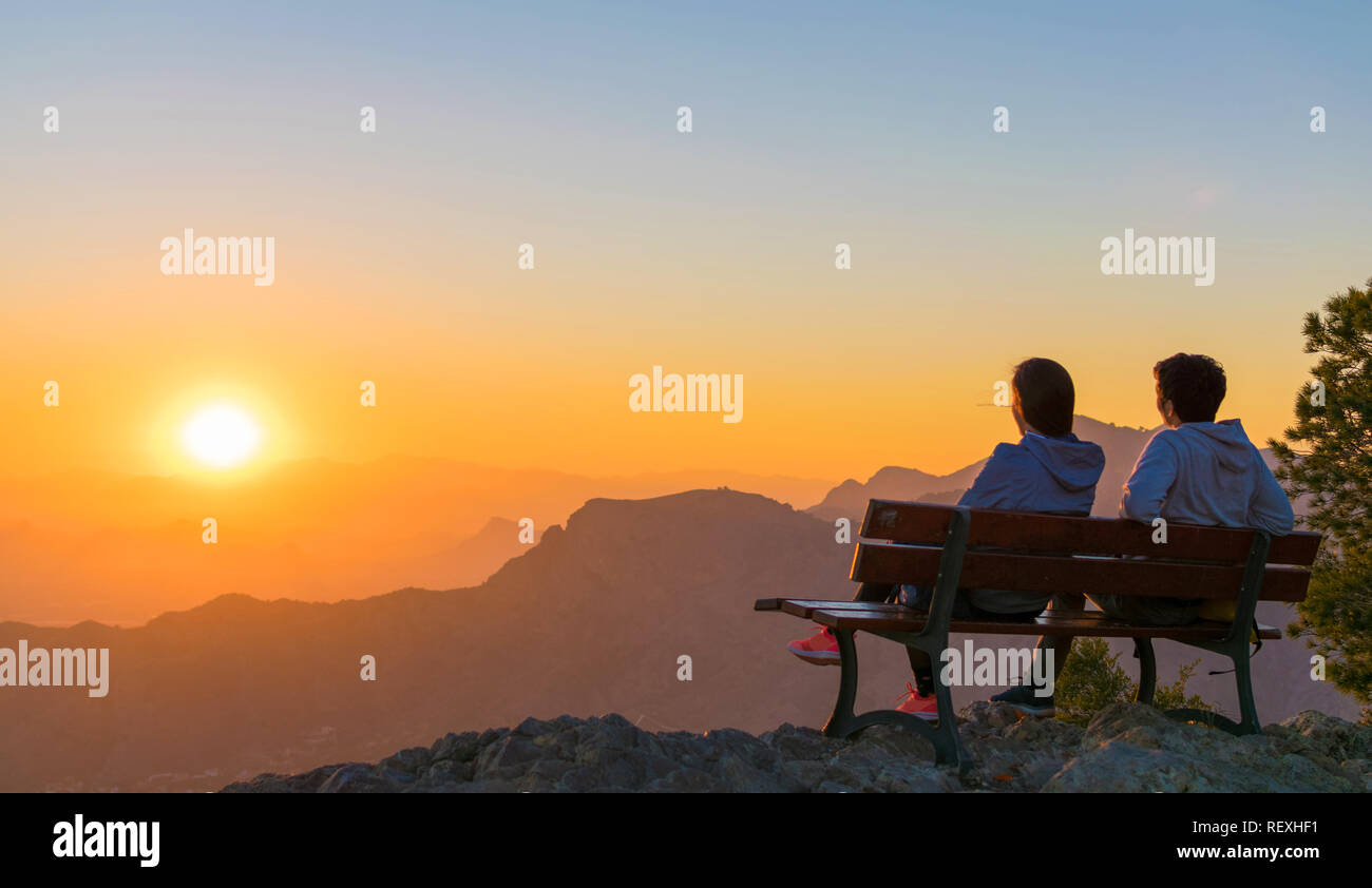 Romantic scene of a couple watching the sunrise in the top of a