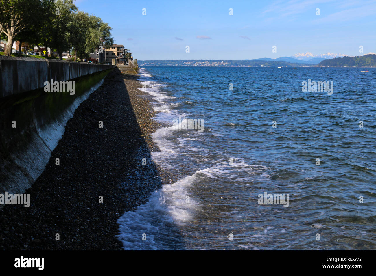 Sea wall at Alki Beach in West Seattle Washington with view of Cascade Mountains in the distance on a sunny day with clear blue sky Stock Photo