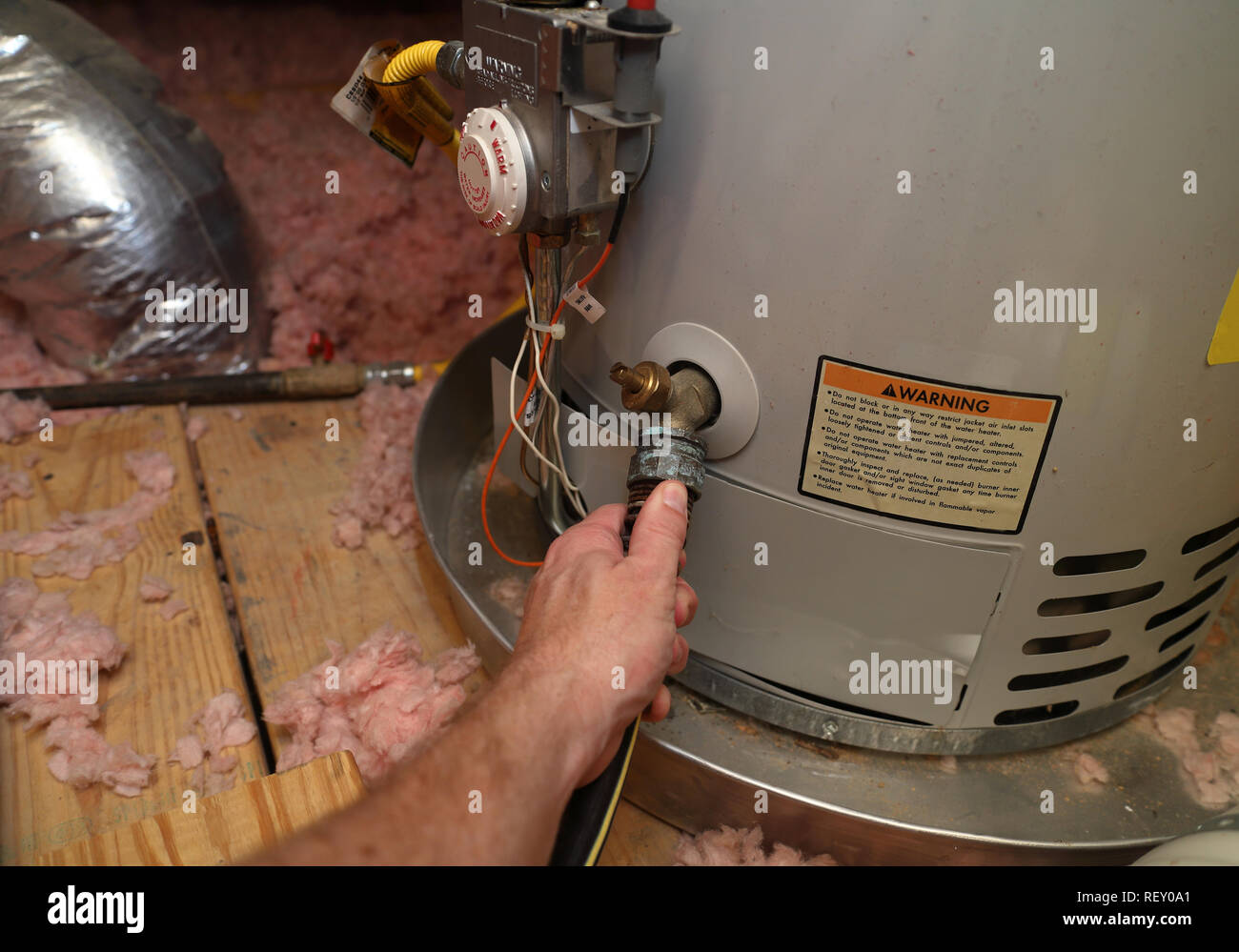 Hand attaches hose to a home water heater to perform maintenance Stock Photo