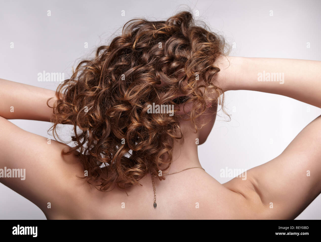 Woman from backside on gray background. Female with curly hair. Stock Photo