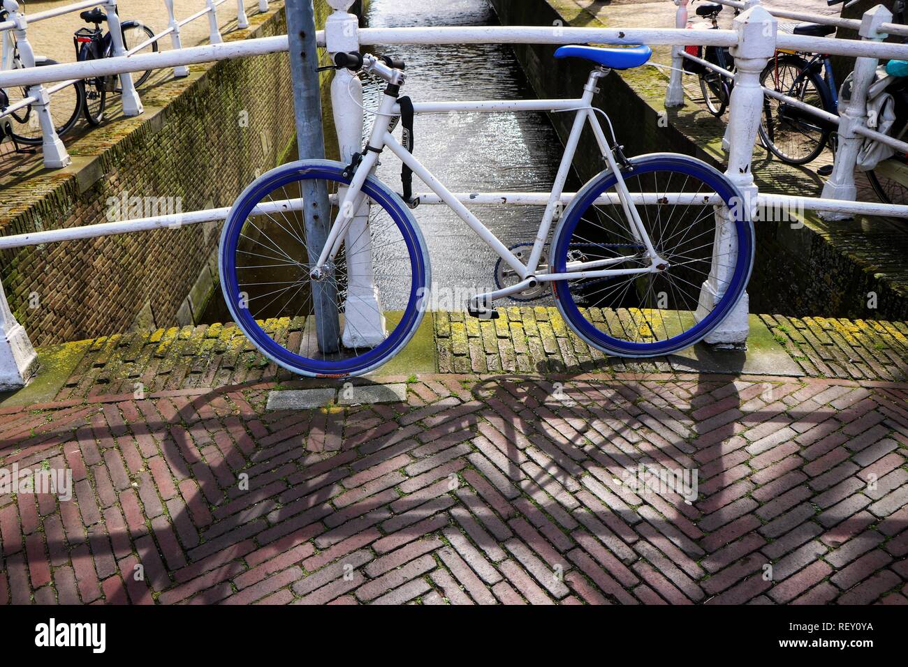 Blue and white bicycle casting a perfect shadow on the cobbles in Amsterdam, The Netherlands. Stock Photo