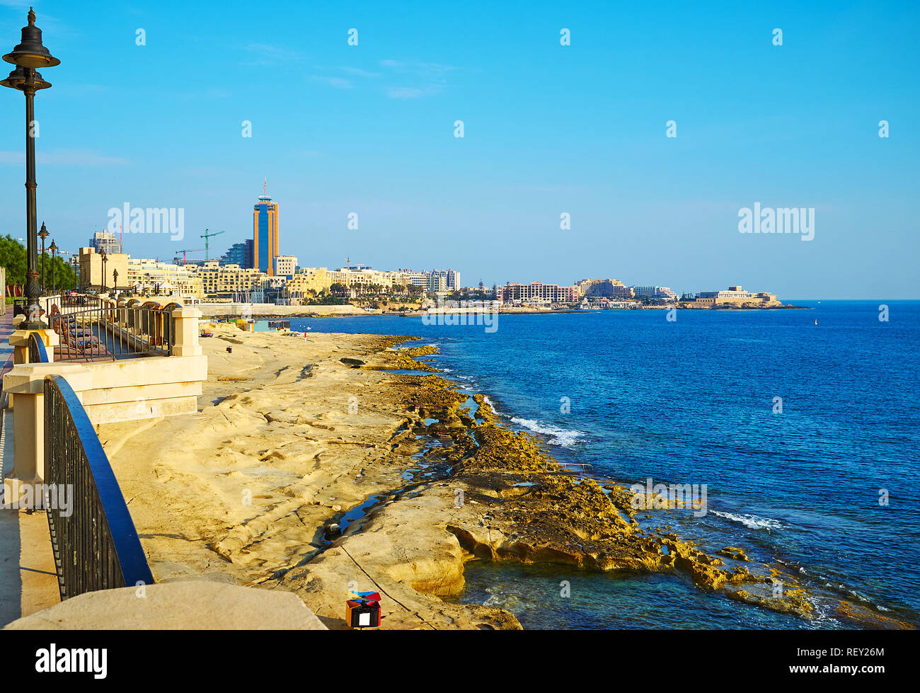The rocky beach of Sliema is stretching along the Tower Road, the modern neighborhood of St Julian's is seen on the background, Malta. Stock Photo