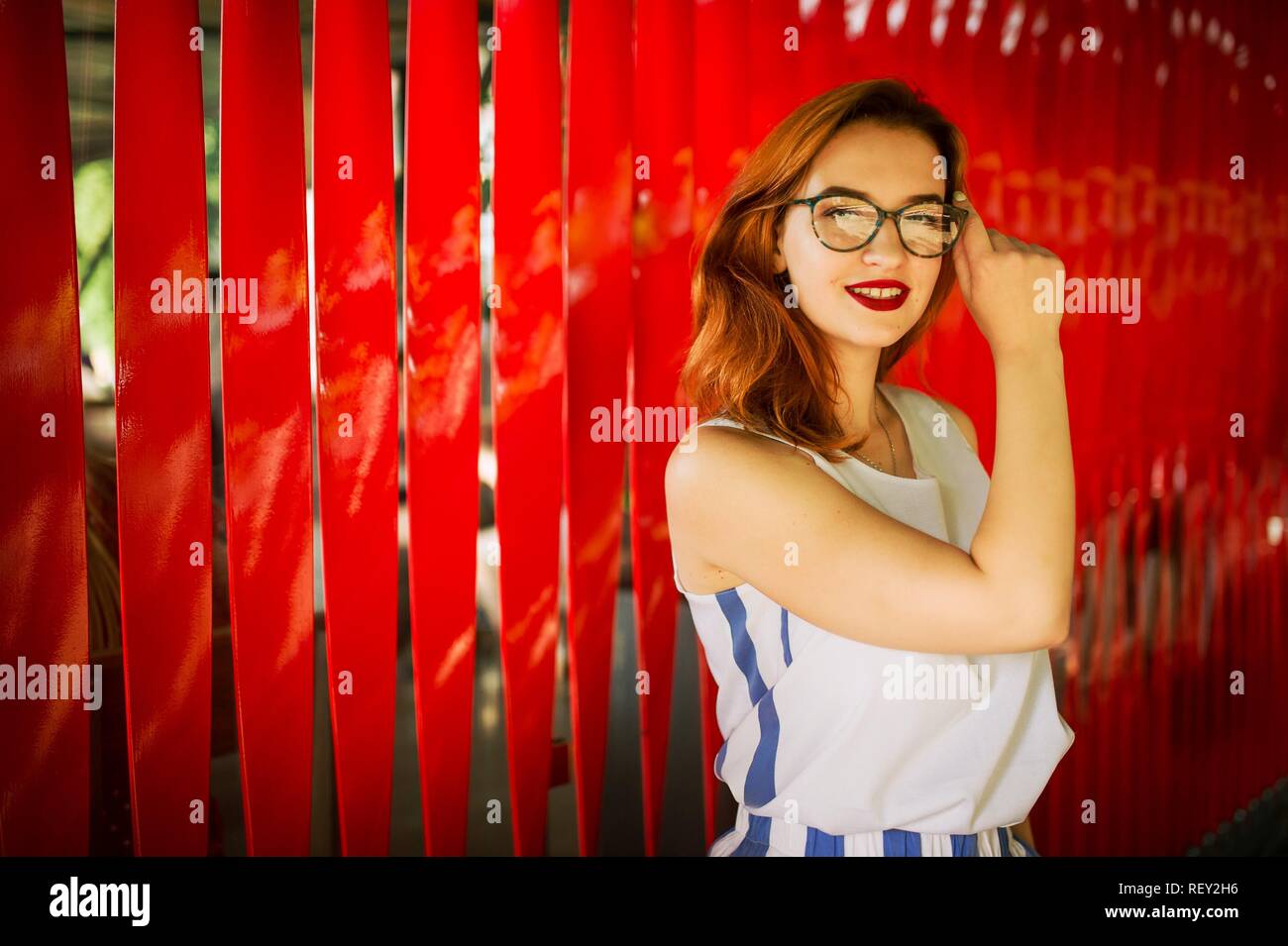 Attractive redhaired woman in eyeglasses posing against red background. Stock Photo