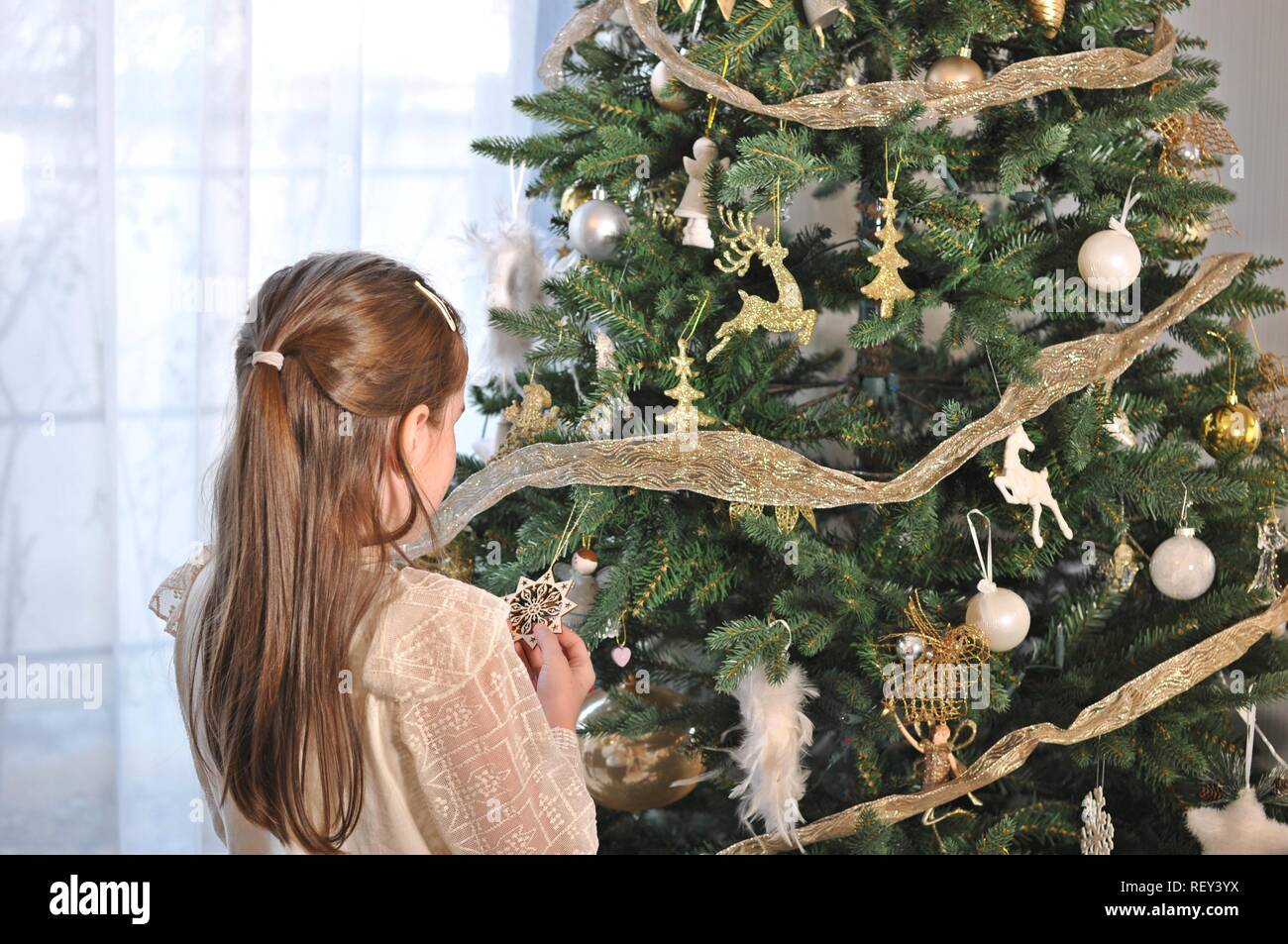 White Caucasian child, girl, standing with the back and decorating the Christmas tree Stock Photo