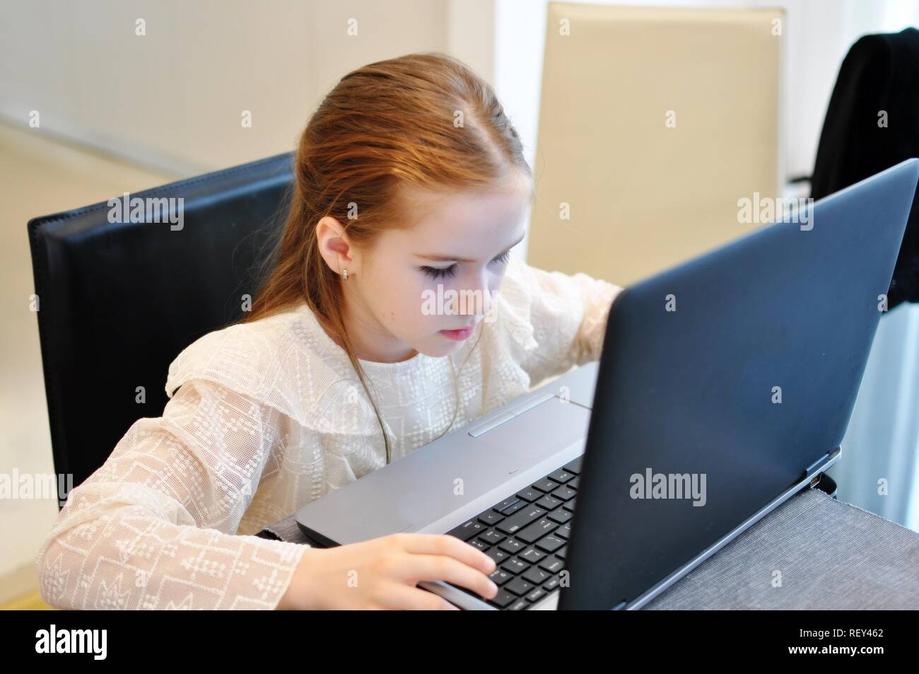 White Caucasian girl (child, kid) sitting in front of the computer and working. Online school due to pandemic. Stock Photo