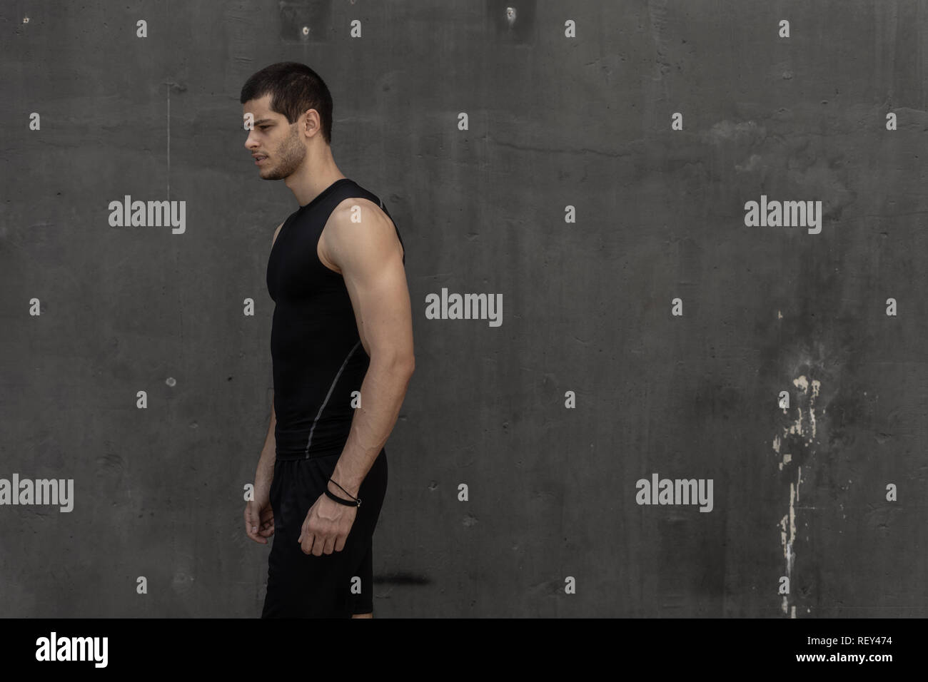 Portrait of athletic muscular young man, in sports clothing, posing on gray industrial background. Fashionable tall male, sport model, muscular body s Stock Photo