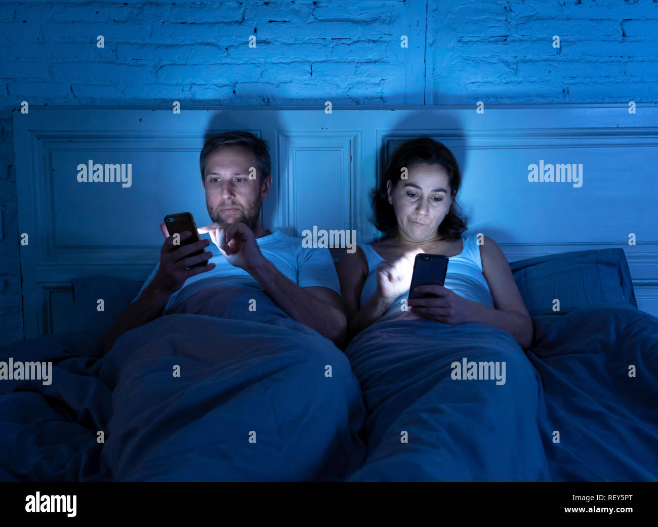 Young couple in bed late at night using smart phones obsessed with games, social media and apps ignoring each other in relationship communication prob Stock Photo