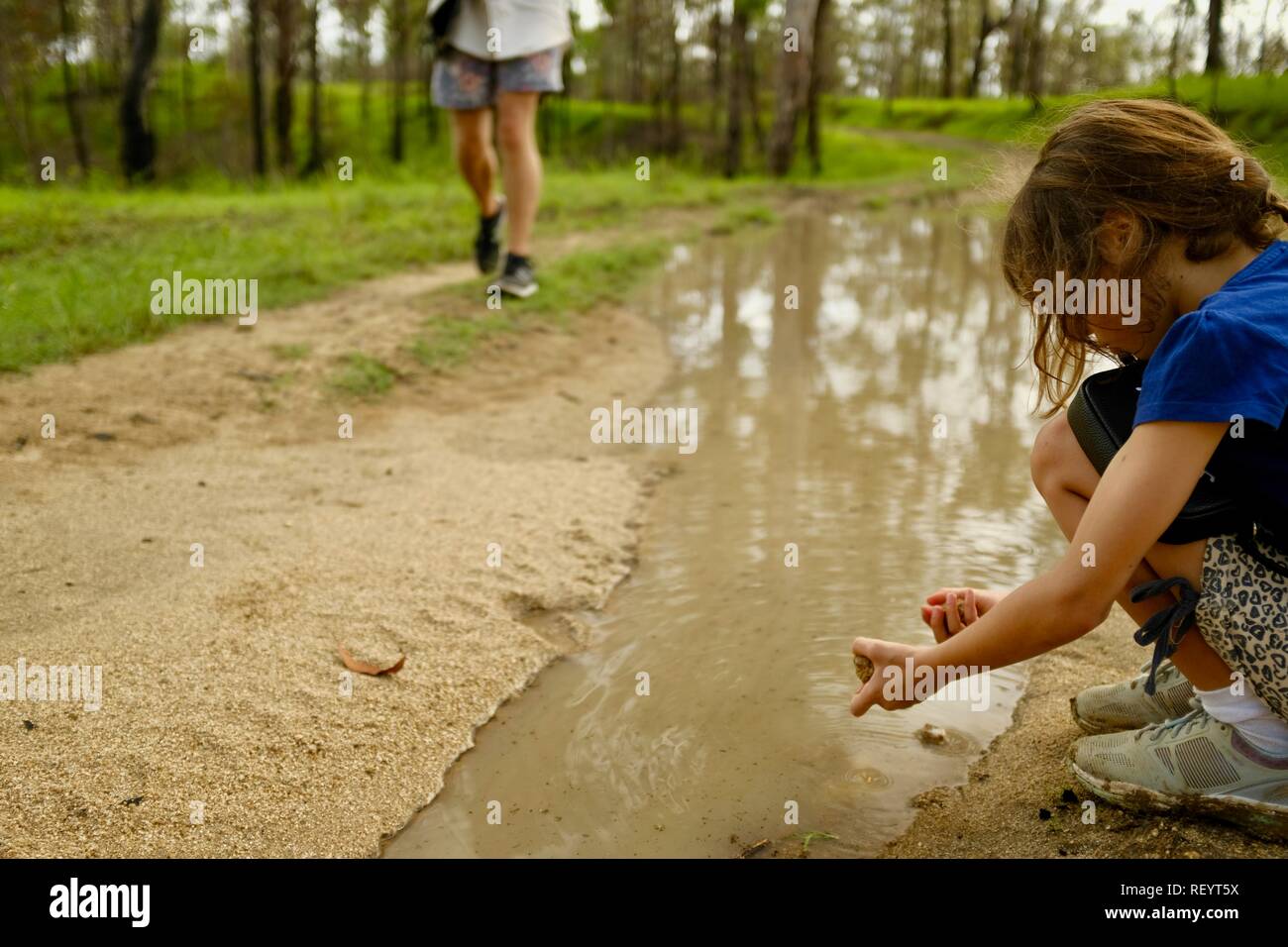A young girl playing in a muddy puddle on a four wheel drive track through a forest, Mia Mia State Forest, Queensland, Australia Stock Photo