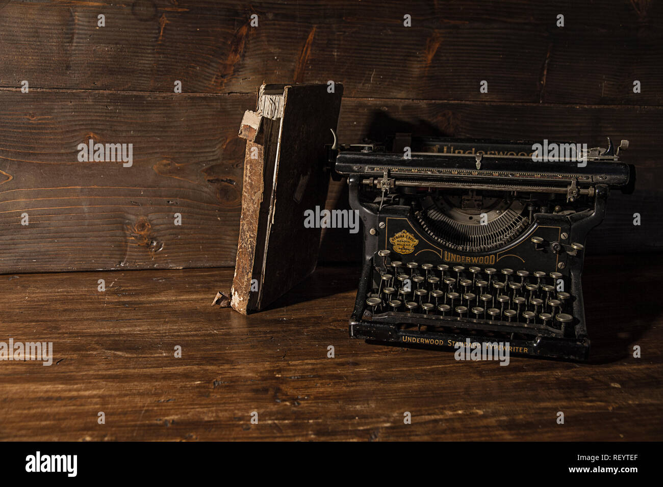 Reading and writing scenes in ancient times: an old book and an old typewriter on a ruined wooden table on a wooden background Stock Photo
