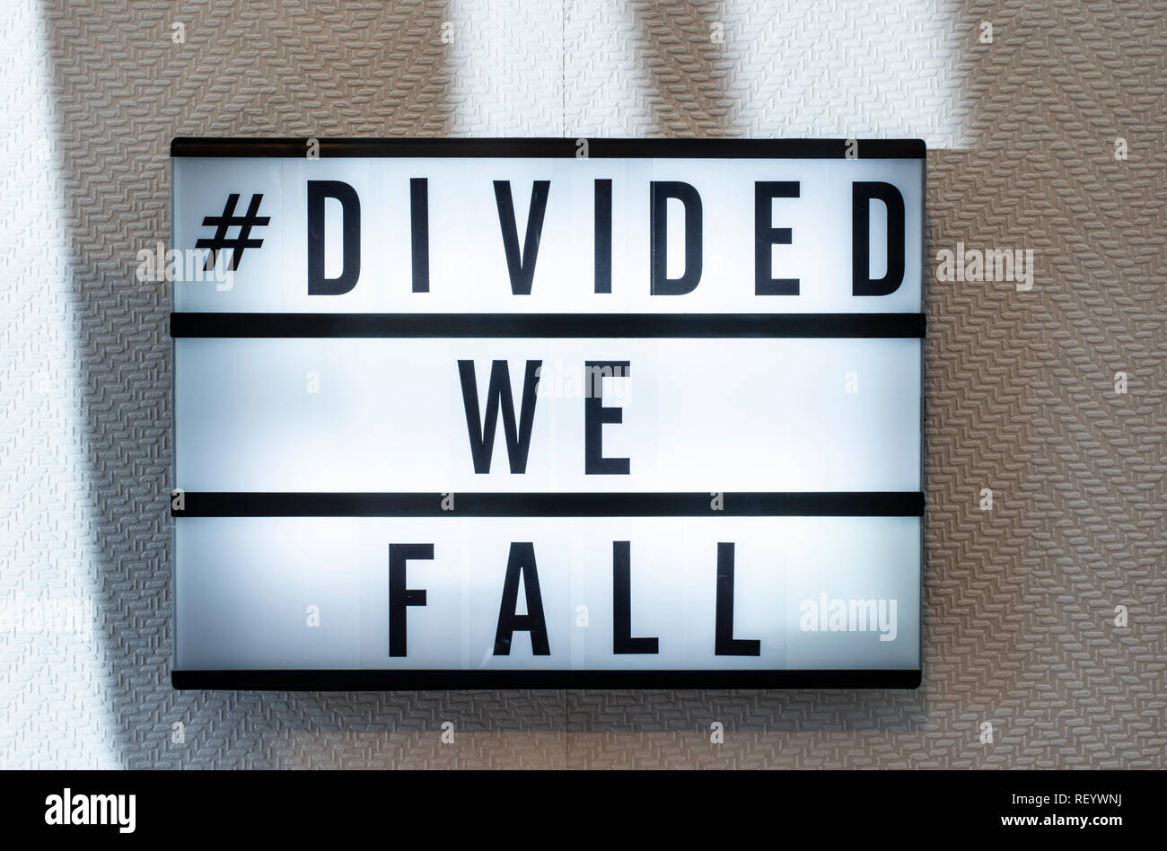 Message divided we fall on illuminated board. Divided nation concept with text. Daylight from window. Room interior. Black letters #divided we fall on Stock Photo