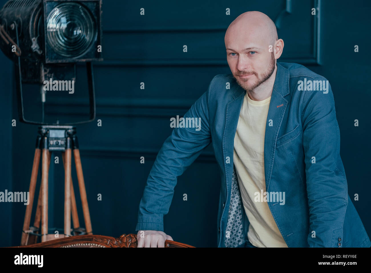 Portrait of attractive adult successful bald bearded man in suit on blue background, blogging, TV host Stock Photo