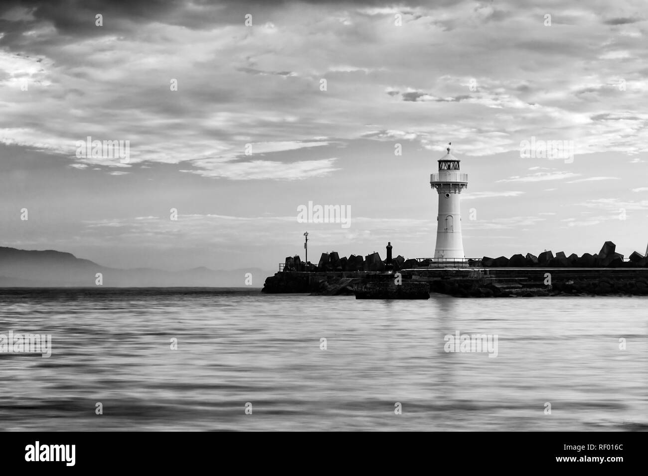 Greyscale impression of white lonely lighthouse on the tip of sandstone breakwater wall protecting Wollongong town harbour from pacific waves. Stock Photo