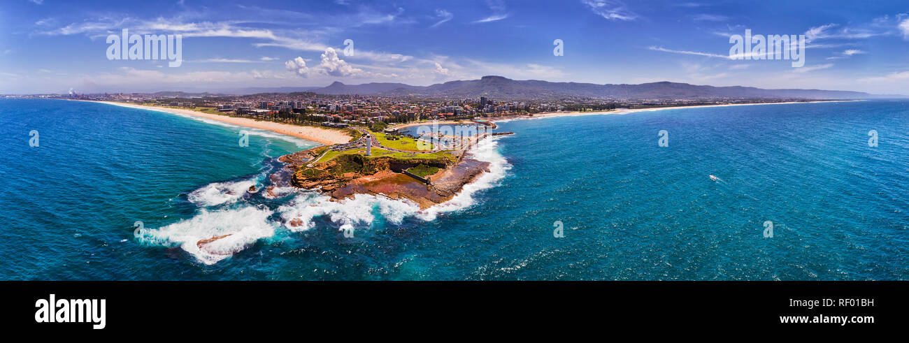 Sandstone headland with white lighthouses and breakwater stone wall protecting Wollongong harbour and marina from wild Pacific ocean waves on Australi Stock Photo