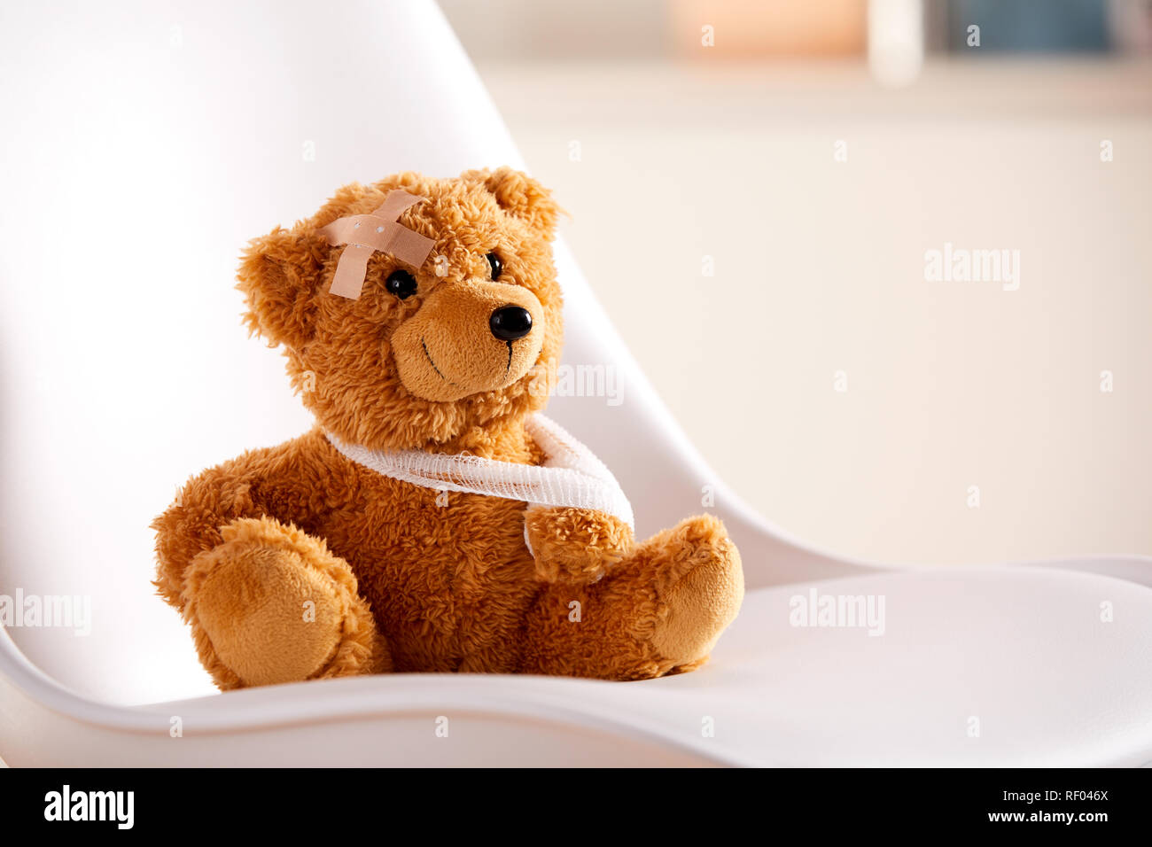 Red Teddy bear toy with a bandaged hand sitting on a chair in close-up on a chair in doctors office. Pediatrics concept with copy space Stock Photo