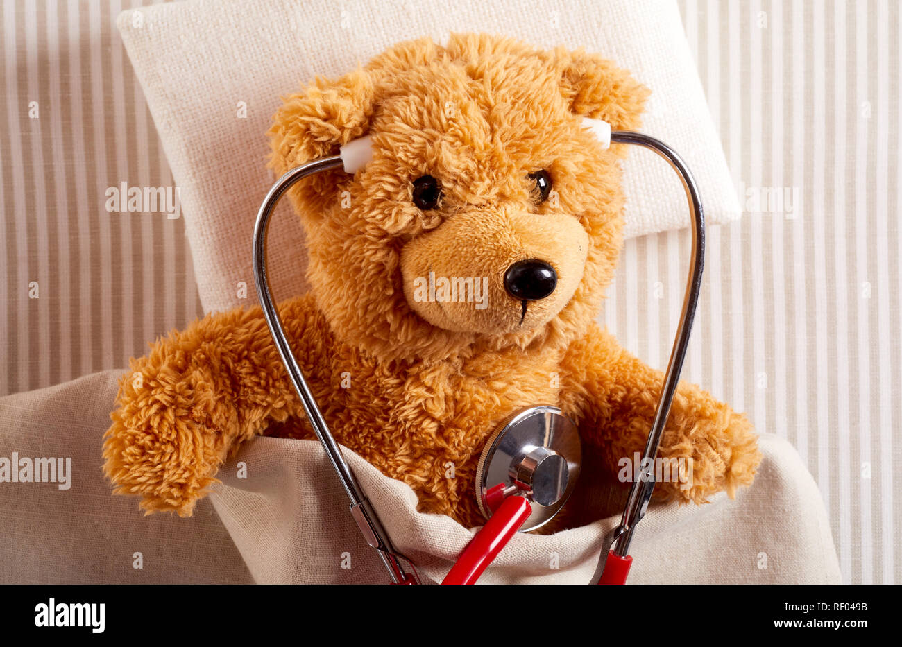 Cute little teddy bear using a stethoscope to listen to its hear as it lies in a hospital bed in a concept of paediatric healthcare Stock Photo