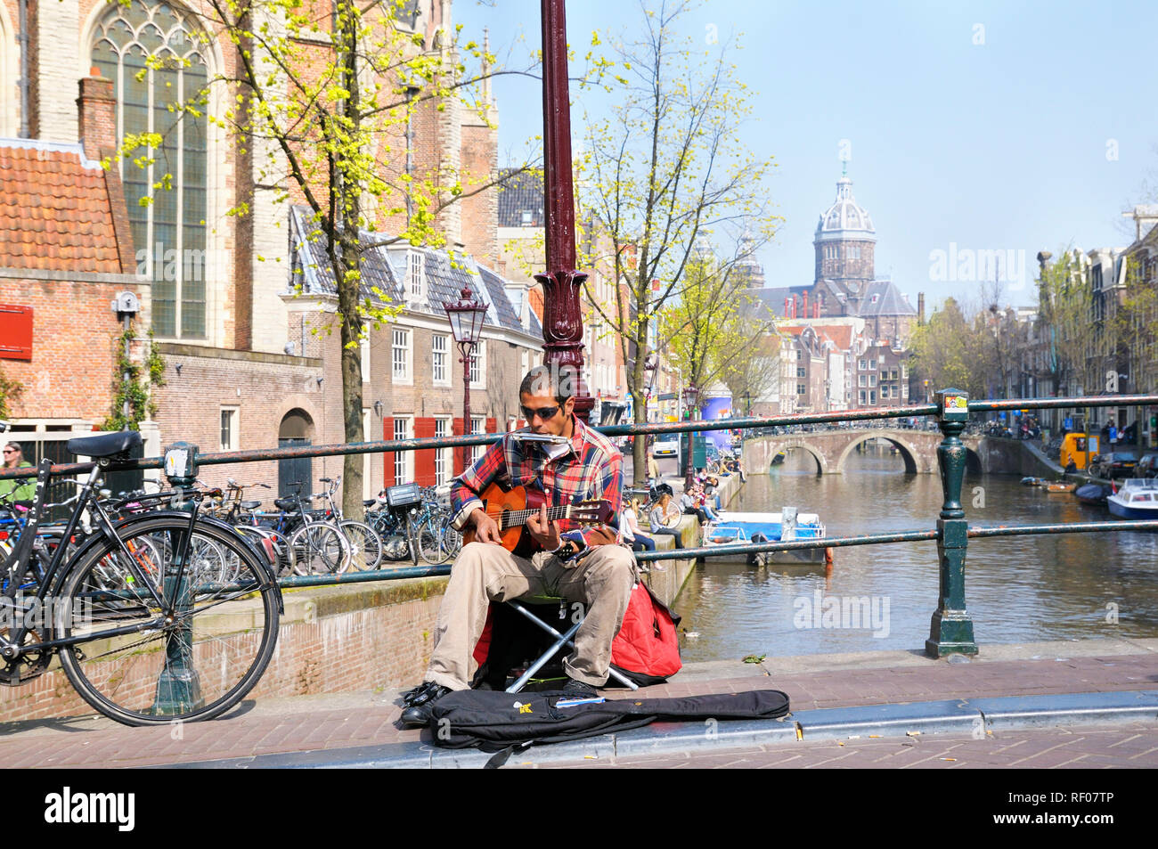 Busker playing guitar and harmonica on a warm spring day in the Red Light District, Amsterdam, North Holland, Netherlands Stock Photo
