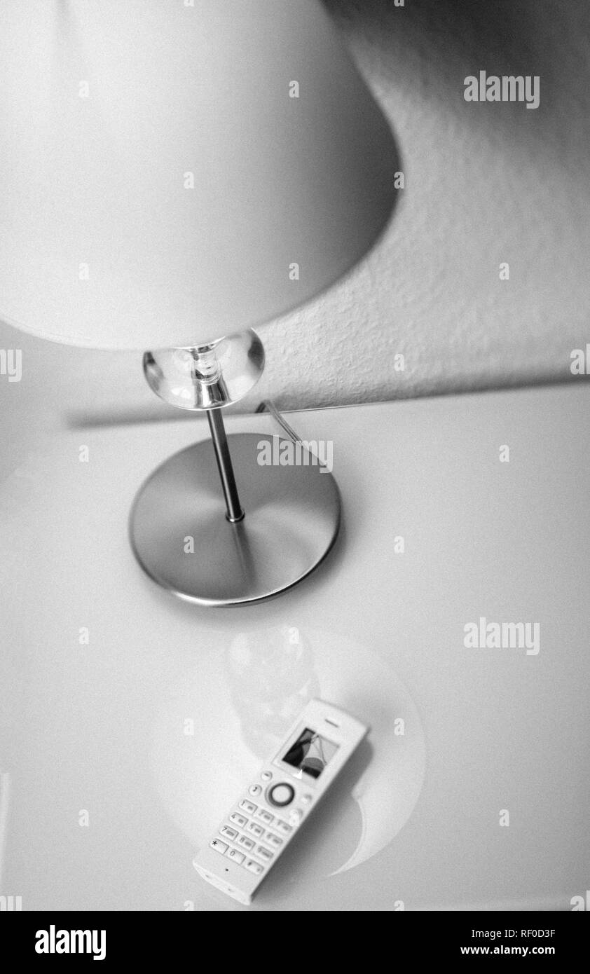 Modern white cordless phone on white living room office interior table next to a desk lamp - view from above of cozy interior decoration - black and white Stock Photo