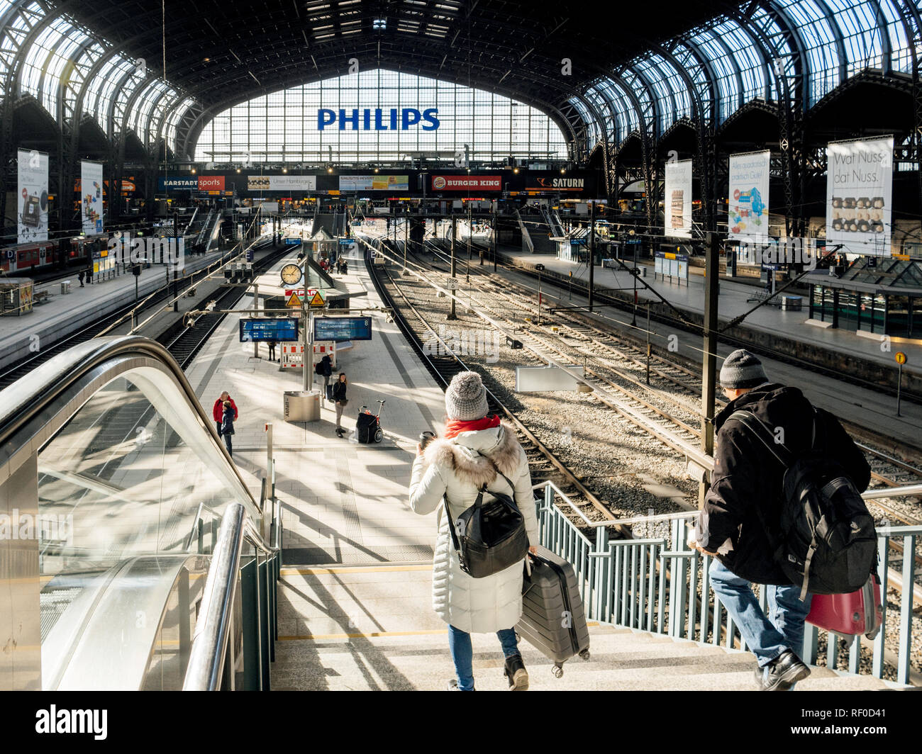 HAMBURG, GERMANY - MAR 20, 2018: Woman and man descending the stairs at Hamburg Hauptbahnhof toward train platform illuminated by sunlight  Stock Photo