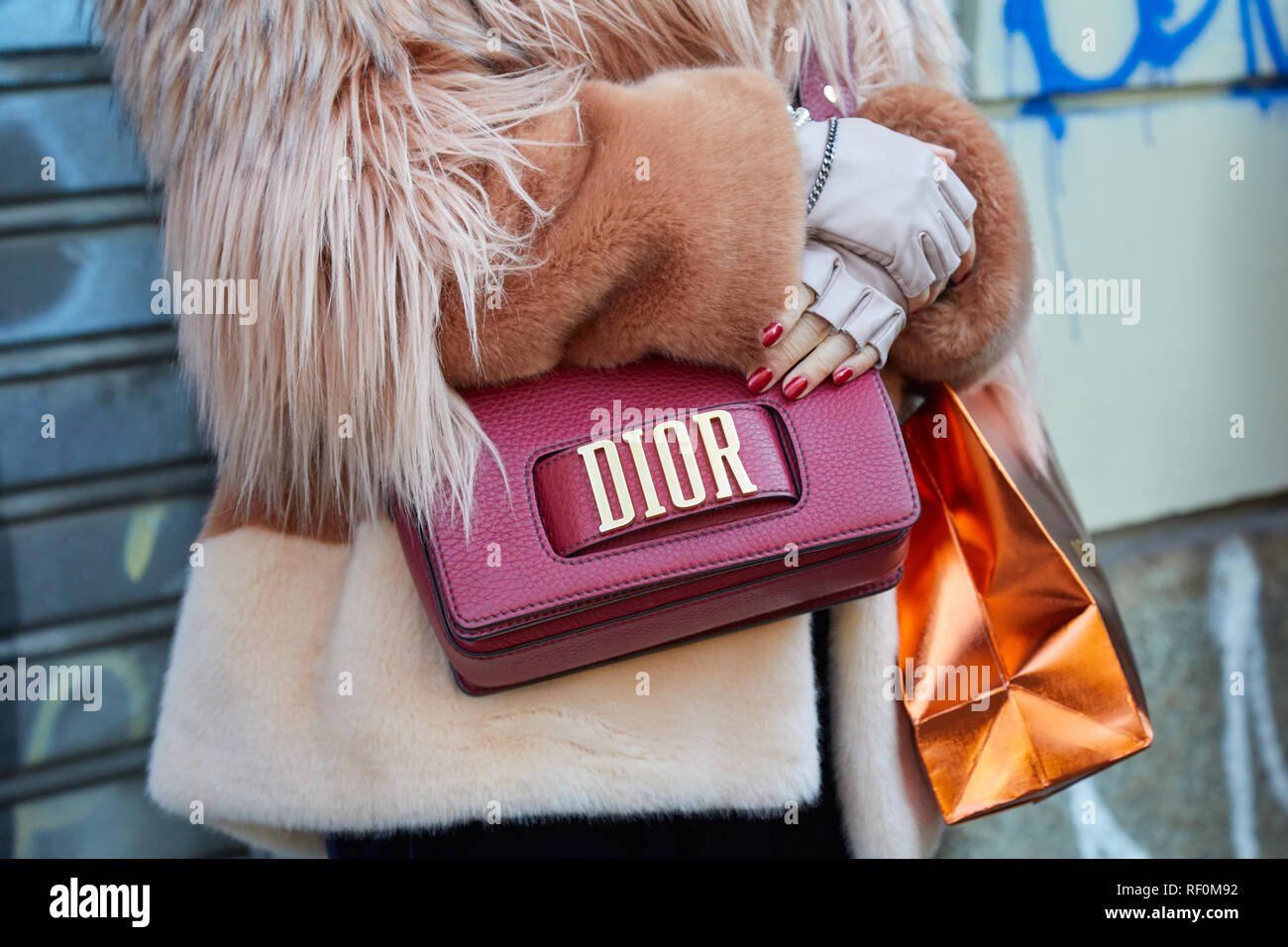 MILAN, ITALY - JANUARY 13, 2019: Woman with red leather Dior bag and brown pink fur coat before John Richmond fashion show, Milan Fashion Week street  Stock Photo