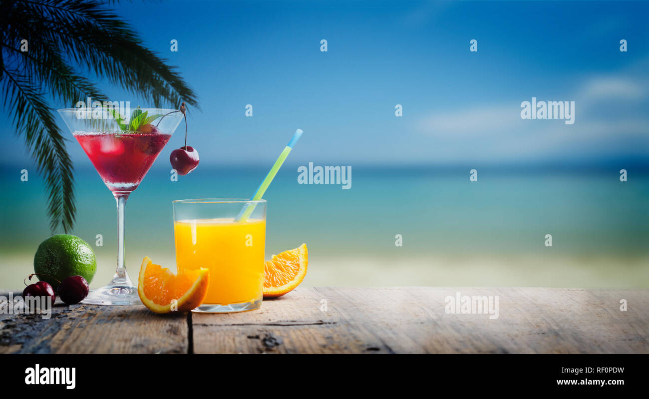 Cherry cocktail in martini glass and orange juice vodka on tropical sandy beach. Summer vacation holiday and beach party design. Island resort beach b Stock Photo