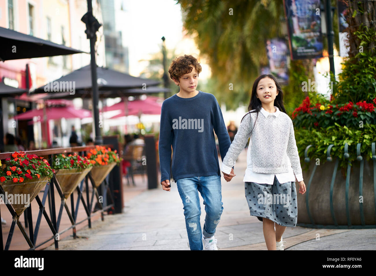 little asian girl and caucasian boy walking together holding hands outdoors Stock Photo