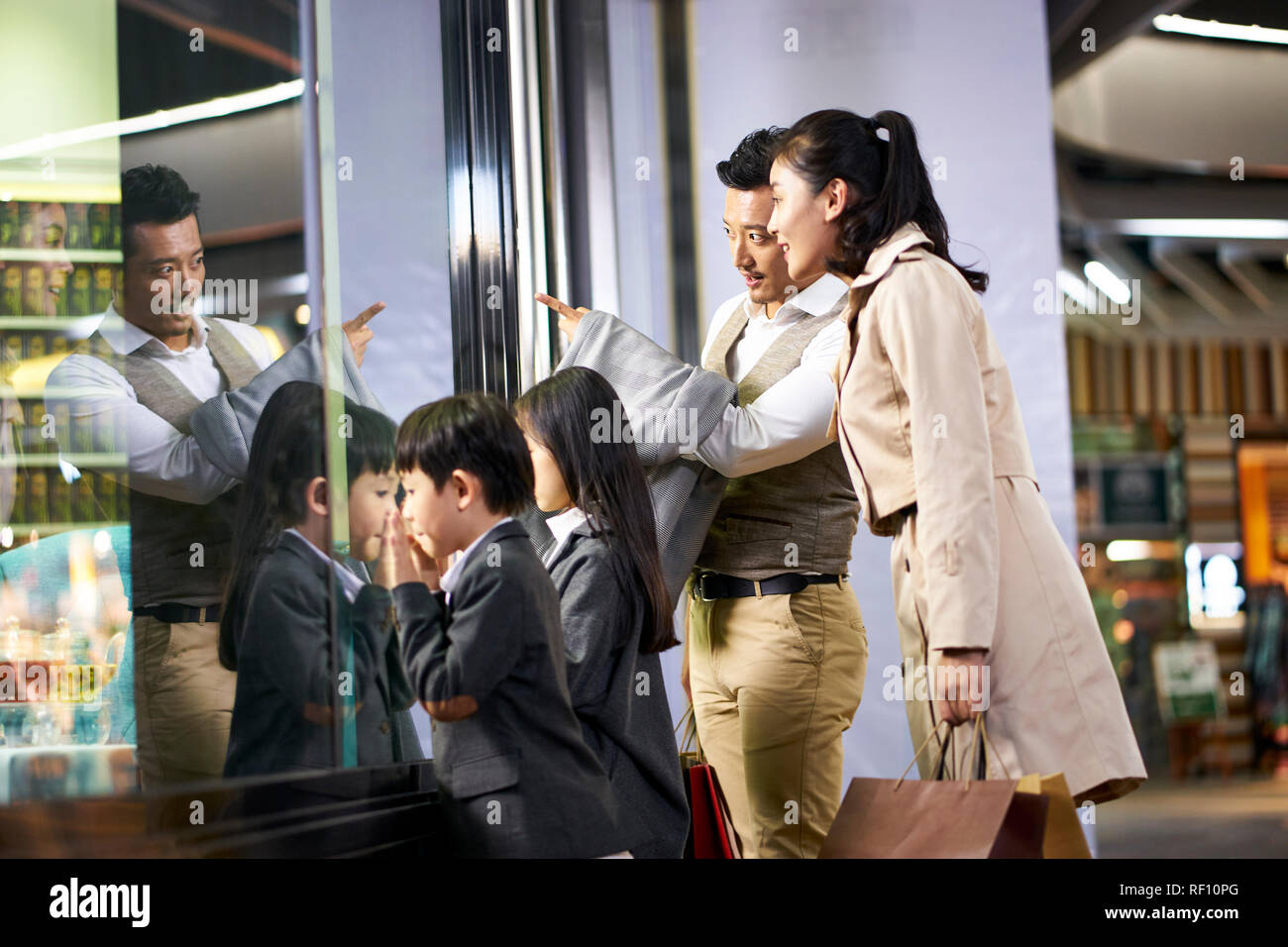 happy asian family with two children looking into a shop window in shopping mall Stock Photo