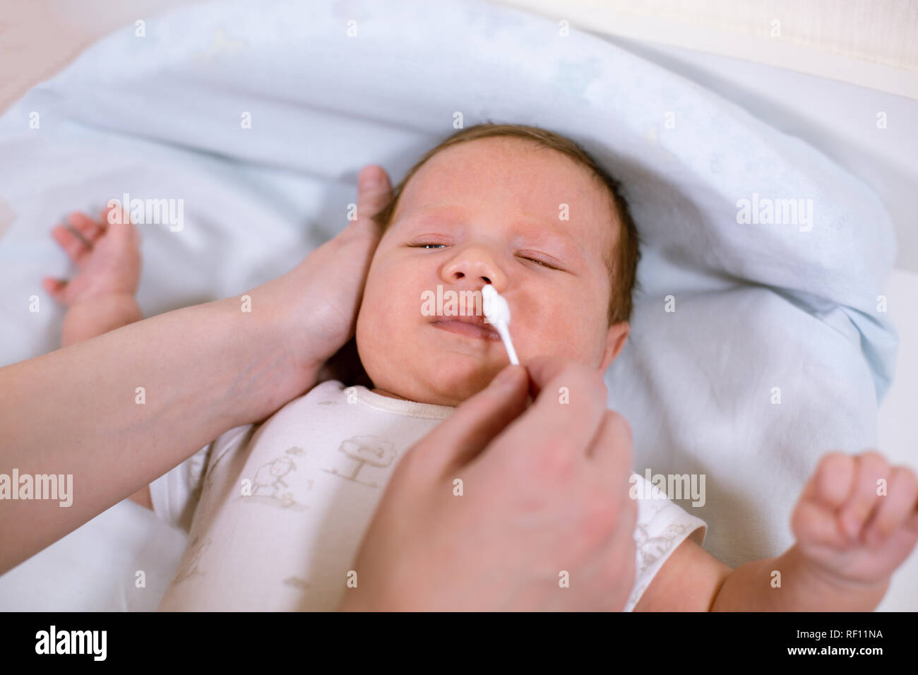 Newborn hygiene. Mother cleaning baby nose with cotton swab, closeup