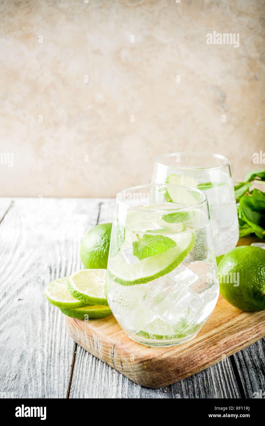 Summer sour drink, with lime and mint, homemade cocktail mojito in two glasses, white wooden background, with fresh limes, mint leaves, ice cubes, cop Stock Photo