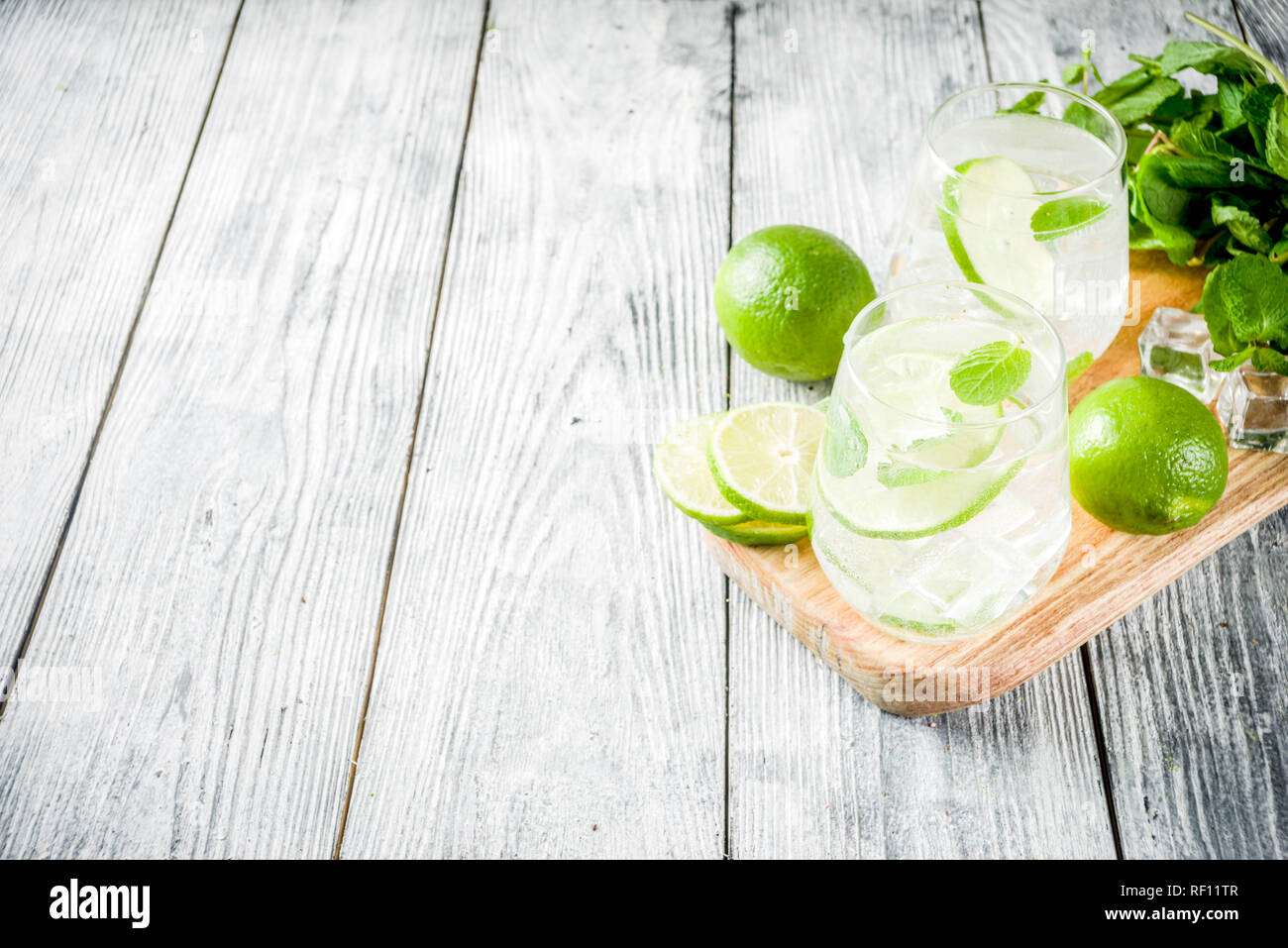 Summer sour drink, with lime and mint, homemade cocktail mojito in two glasses, white wooden background, with fresh limes, mint leaves, ice cubes, cop Stock Photo