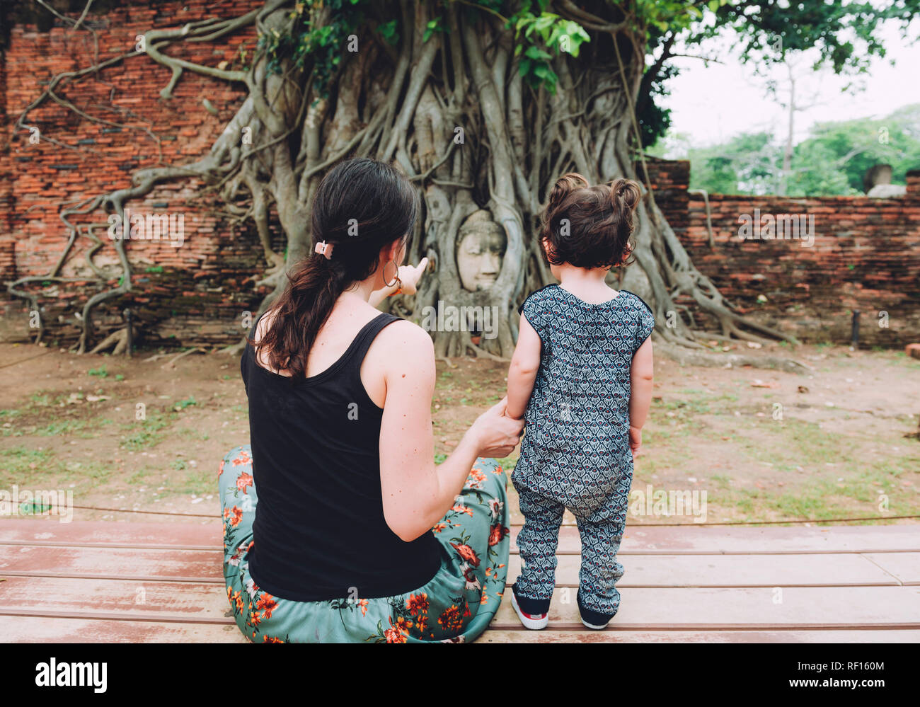 Thailand, Ayutthaya, Mother and daughter visiting the Buddha head in between tree roots at Wat Mahathat Stock Photo