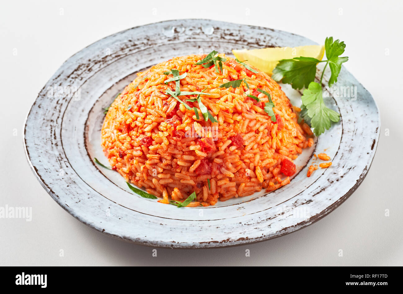 Serving of healthy nutritious Greek tomato pilaf with long grained rice and fresh coriander on an old rustic pottery plate Stock Photo