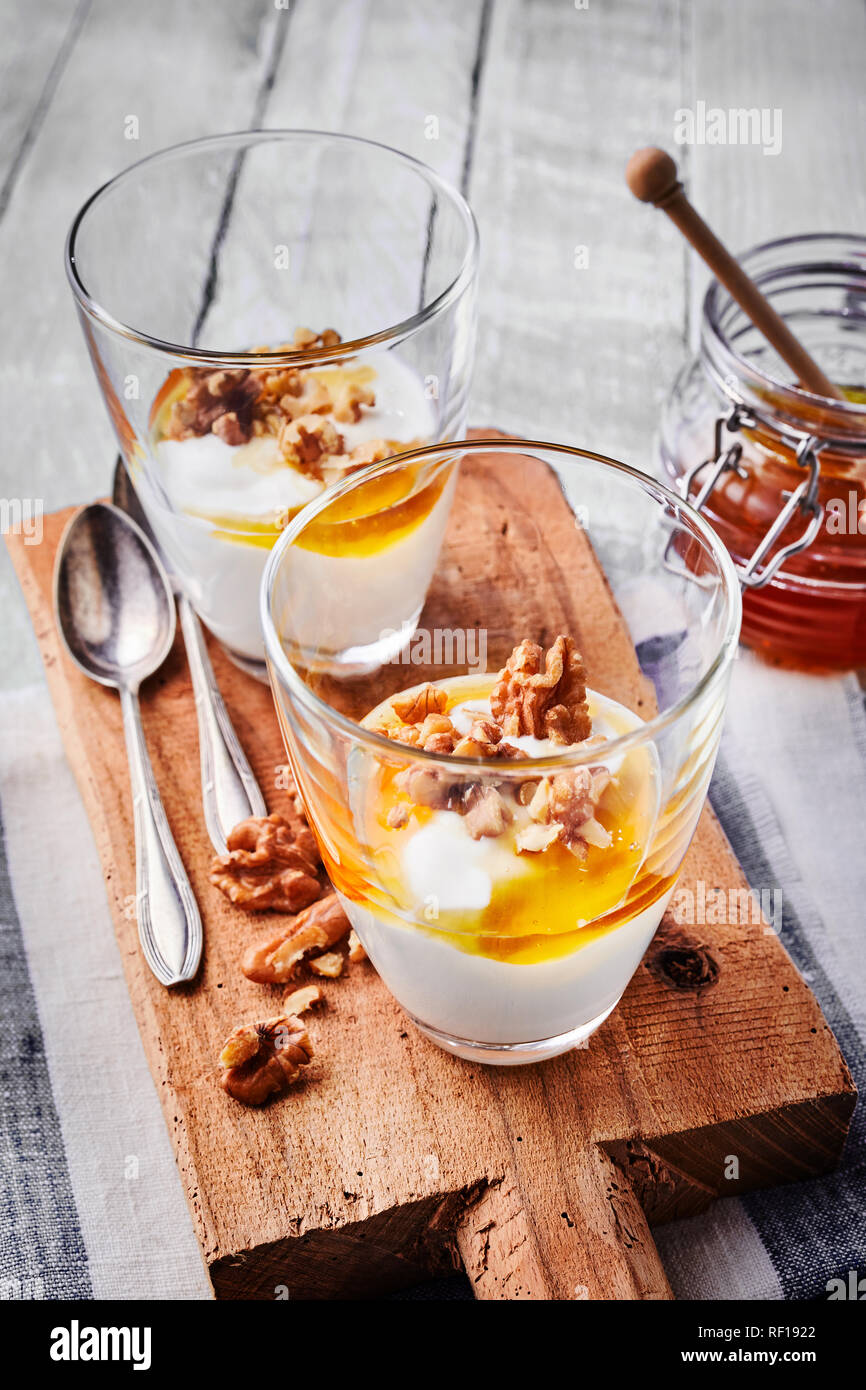 Healthy fresh Greek yogurt dessert or breakfast topped with walnuts and honey and served in individual glasses on a rustic wooden board Stock Photo