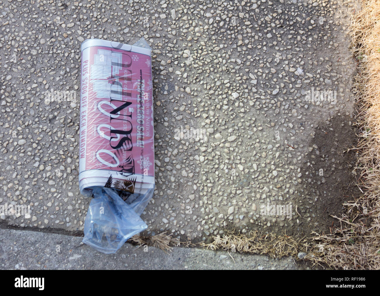 Baltimore Sun newspaper's free SUNPlus advertising supplement bagged in plastic on semi-wet sidewalk / pavement beside grass lawn, Baltimore, Maryland Stock Photo