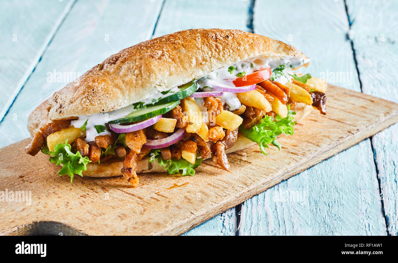 Delicious Greek gyros burger with roasted meat sliced from a kebab, potato chips, fresh salad trimmings on a crusty bread roll served on a board Stock Photo