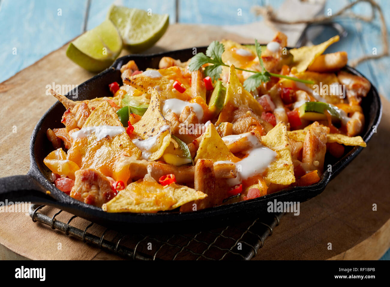 Spicy Mexican chicken with nachos and fresh herbs drizzled with cream and served in a rustic skillet in a close up view Stock Photo