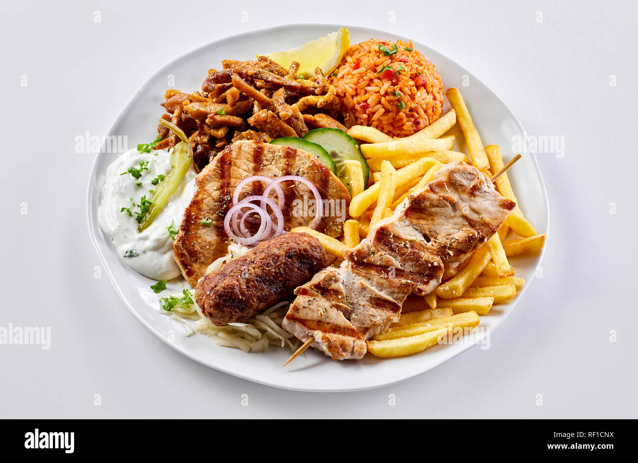 Regional Greek mixed grill with fried potato chips and tomato pilaf with souvlaki, souzuki steak and pork skewers served with raita Stock Photo