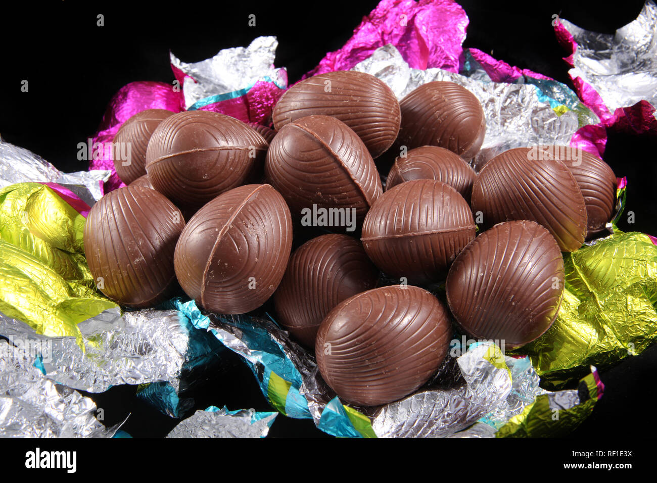 Pile of unwrapped chocolate easter eggs with the colorful foil wrapping surrounding it on a black background. Stock Photo