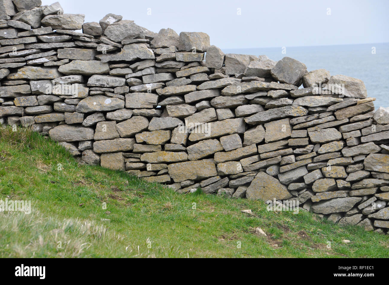 Dry stone wall on the Isle of Purbeck, Dorset. Rough limestone wall divides sloping coastal fields with the sea in the background. Stock Photo