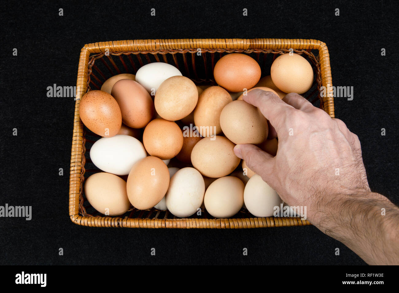 Top view of a male hand taking a hen egg from a basket on a black background Stock Photo